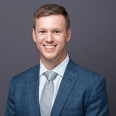 A professional headshot of Dan with a gray background.