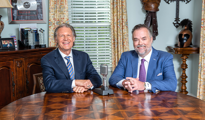 A professional photo of Tony and Phillip sitting at a table with a microphone in front of them.