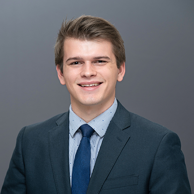 A professional headshot of Trevor with a gray background.